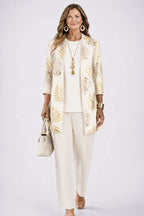 Woman in a cream cardigan with gold metallic leaf print, worn over an ivory top and matching trousers