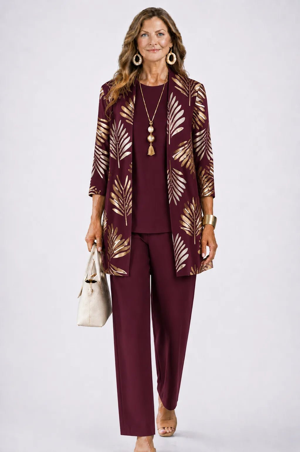 Woman wearing a burgundy longline cardigan with gold leaf print, paired with a burgundy top and matching trousers