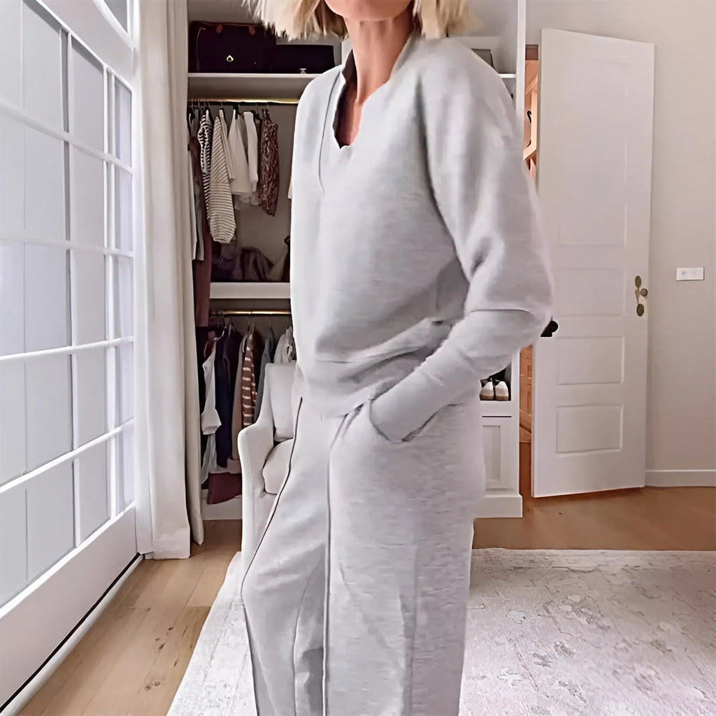 Close side view of the heather grey ribbed V-neck collar and relaxed jumper fit against a bright window