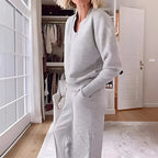 Close side view of the heather grey ribbed V-neck collar and relaxed jumper fit against a bright window