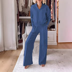 Model in a slate blue V-neck jumper and matching wide-leg trousers standing in a bedroom with an open wardrobe
