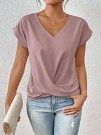 Close-up of a woman wearing a dusty pink V-neck top with cap sleeves and a twist-front hem, paired with jeans