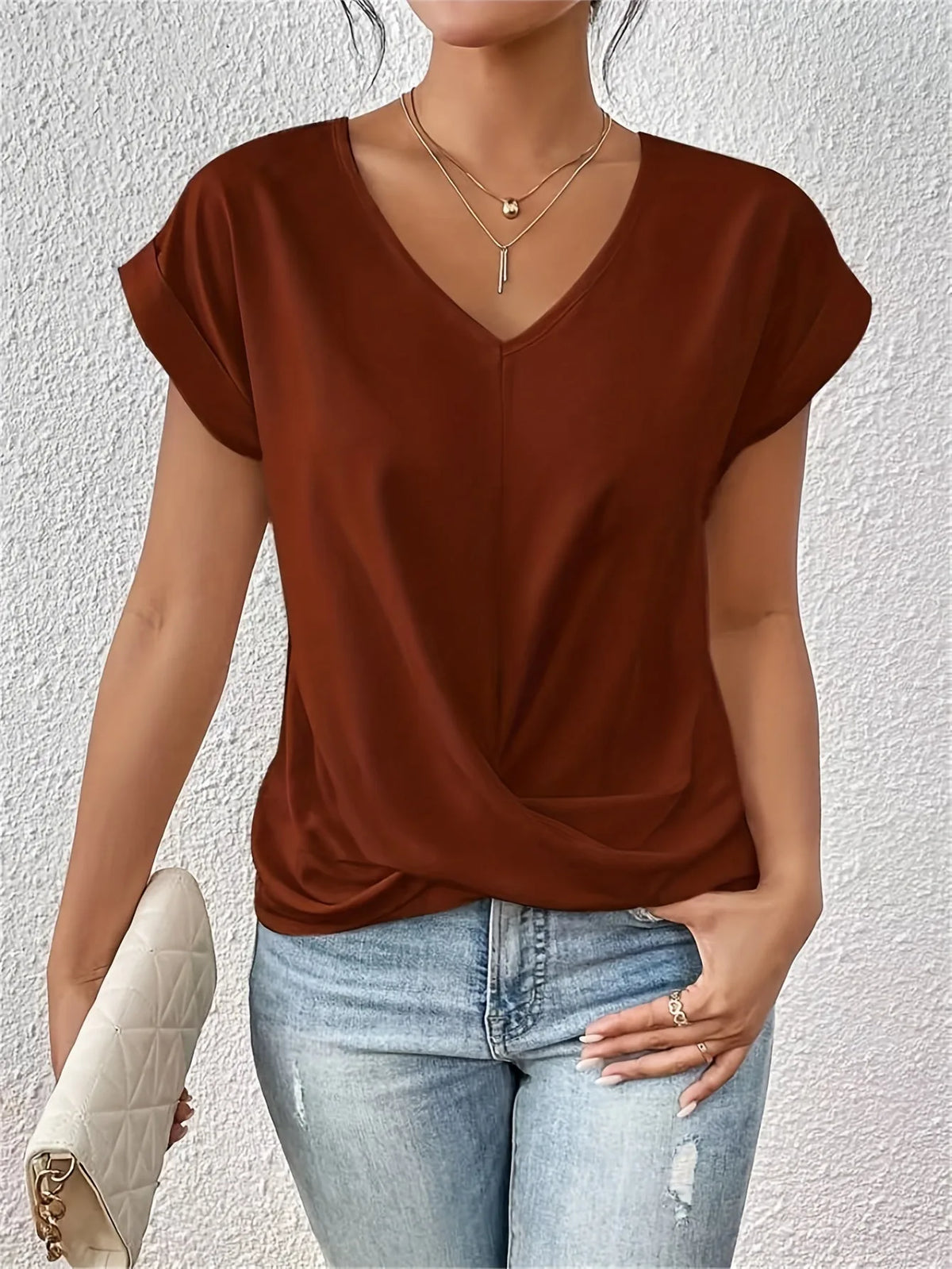 Rust brown V-neck top with cap sleeves and draped twist-front styling, worn with ripped denim jeans