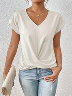 Off-white V-neck top with relaxed cap sleeves and a gathered twist-front hem, paired with light denim