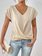Beige V-neck top with cap sleeves and twist-front hem, styled with a quilted cream handbag and jeans