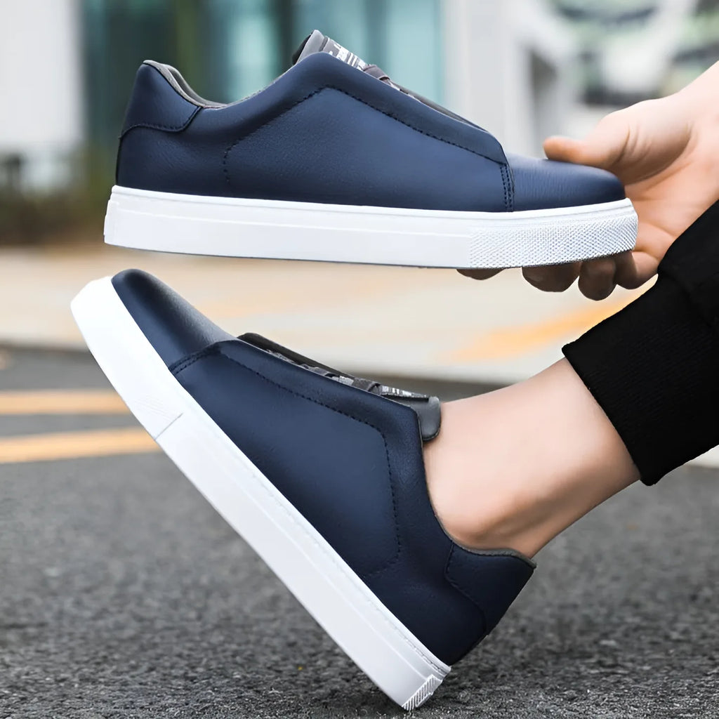 Navy blue leather trainer held in hand above a matching pair worn on foot outdoors