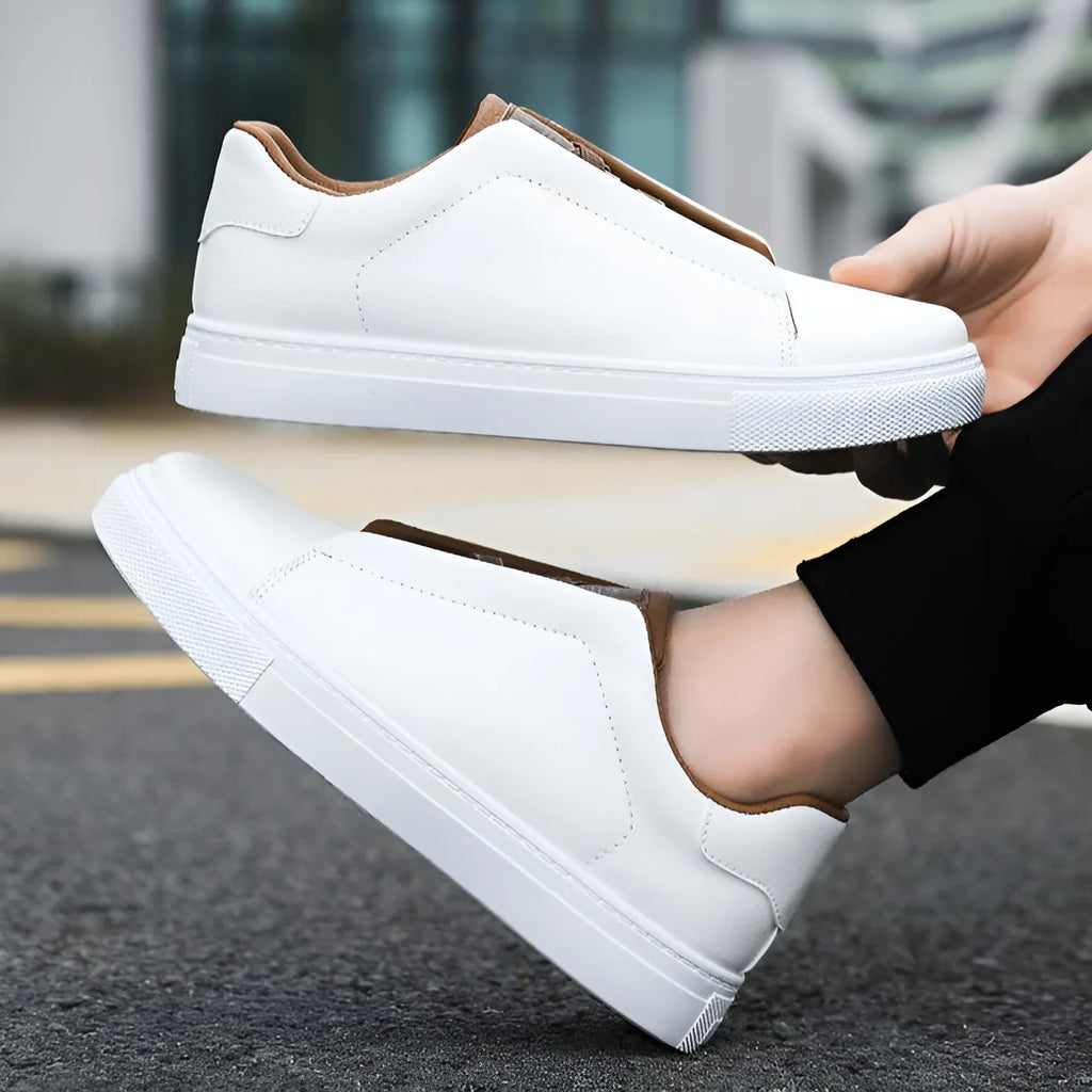 White leather trainer held in hand above its matching pair worn on foot on a street
