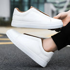 White leather trainer held in hand above its matching pair worn on foot on a street