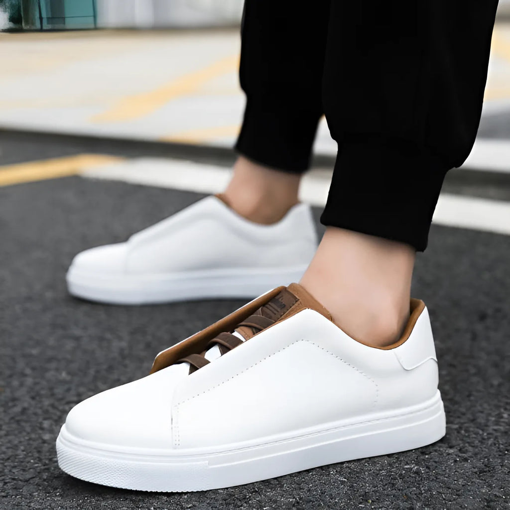White leather trainer with tan trim worn on foot, paired with black trousers, side angle