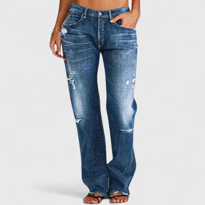 Close-up front view of mid-blue whiskered denim with hand in pocket showing distressed thigh rips