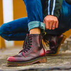 Close-up of crimson red leather lace-up boots worn with cuffed jeans while crouching outdoors