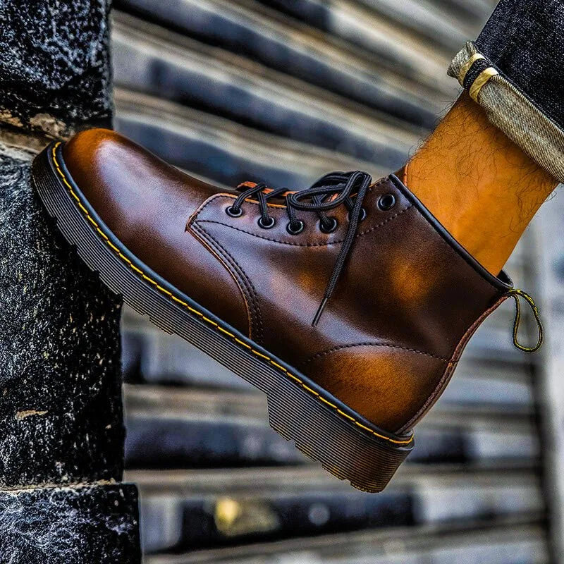 Detail shot of ember brown leather boot worn on foot, showing stitched sole and pull tab on a stone ledge