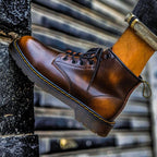 Detail shot of ember brown leather boot worn on foot, showing stitched sole and pull tab on a stone ledge