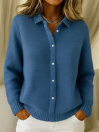 Mid-blue waffle-knit cardigan close-up showing ribbed cuffs and hem detail with hands resting in trouser pockets.