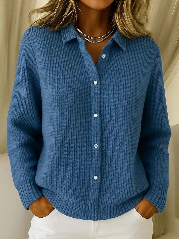 Mid-blue waffle-knit cardigan close-up showing ribbed cuffs and hem detail with hands resting in trouser pockets.