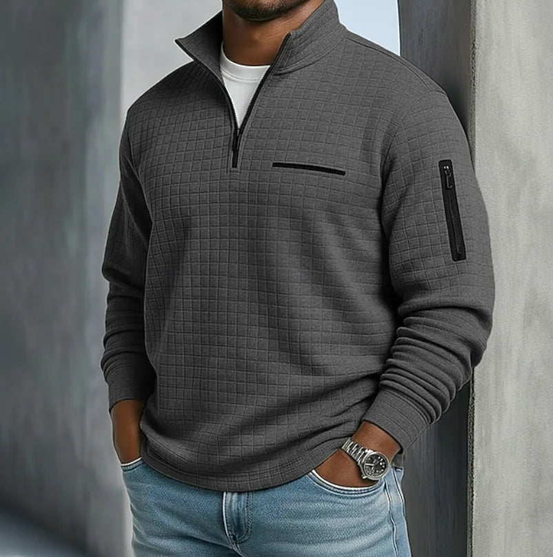 Charcoal grey waffle-texture quarter-zip jumper with black zip detailing against a concrete backdrop