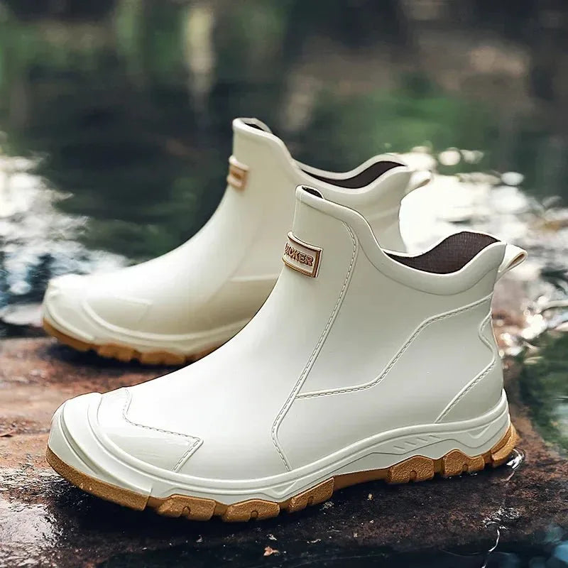 Pair of beige chelsea rain boots with tan tread sole shown by a reflective pond
