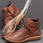Side view of brown leather ankle boots with looped buckle strap detail and a splash of water demonstrating waterproof finish