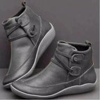 Grey leather ankle boots shown from the side with round toe, contrast white sole and criss-cross strap buckle