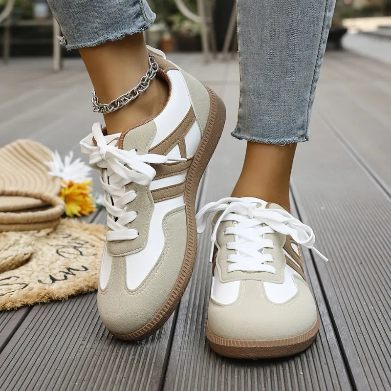 Close-up side view of white and taupe suede panel trainers with chunky lace-up front, worn with cropped jeans and a chain anklet