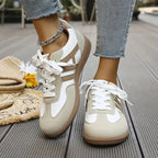 Close-up side view of white and taupe suede panel trainers with chunky lace-up front, worn with cropped jeans and a chain anklet