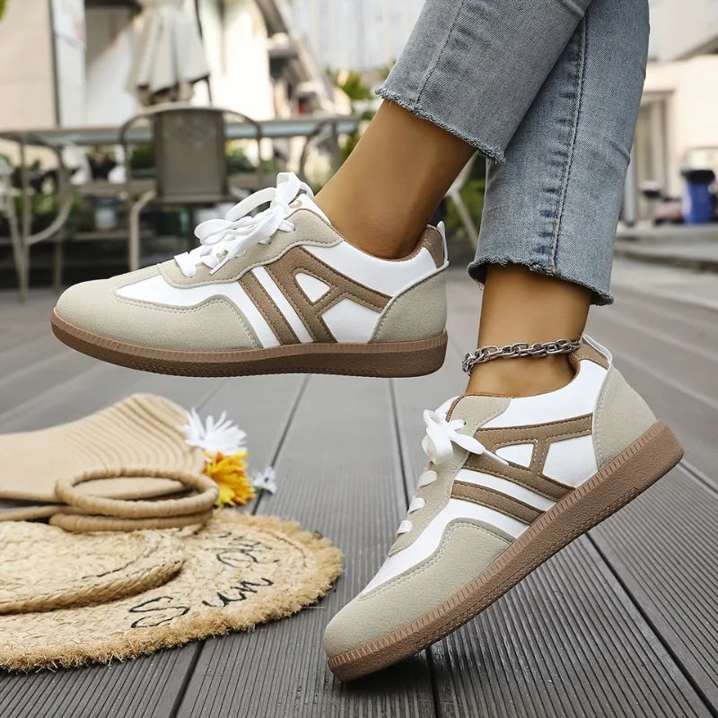 Front angled view of a white and beige trainer with an A-shaped taupe suede panel across the toe box