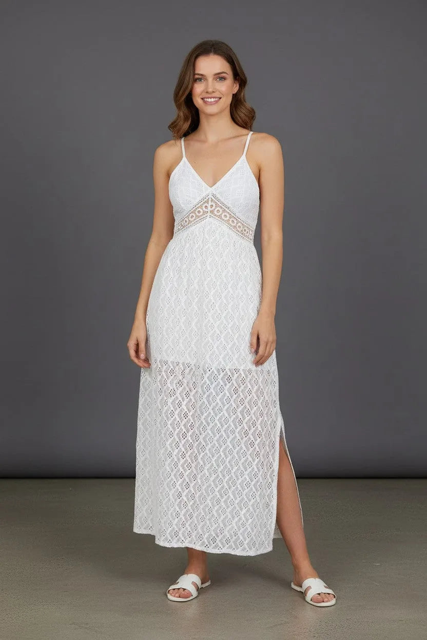 Front view of a woman wearing a white lace maxi dress with thin straps and a V-neckline against a grey backdrop