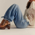 Close-up of the tied drawstring cuff detail at the ankle, seated pose showing the balloon-leg silhouette