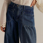 Close-up of the buttoned patch pockets and gathered waistband detail on dark blue denim trousers