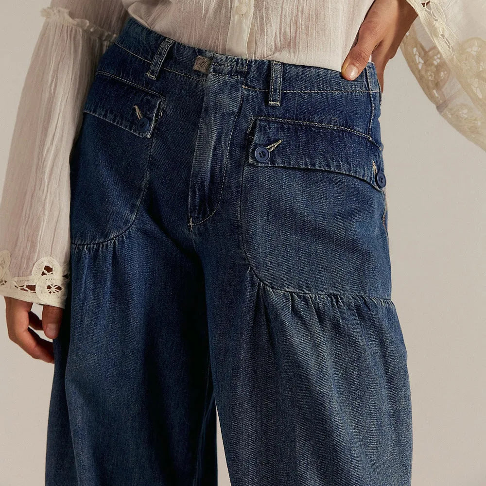 Close-up of the buttoned patch pockets and gathered waistband detail on dark blue denim trousers