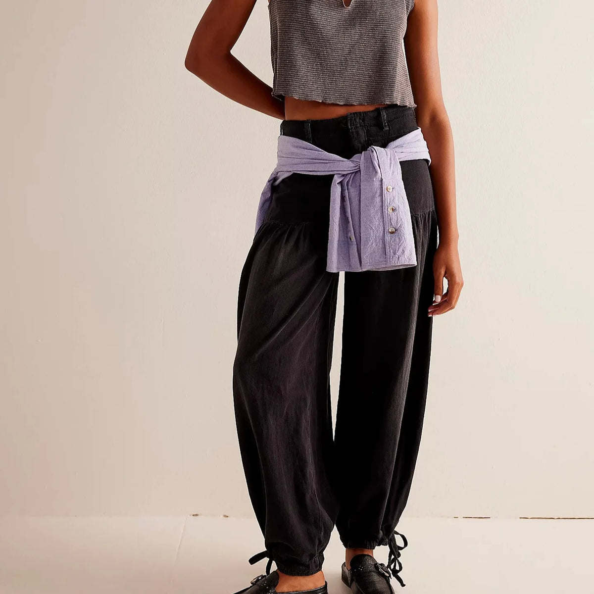 Front view of black wide-leg trousers with elastic drawstring cuffs, styled with a knotted top at the waist