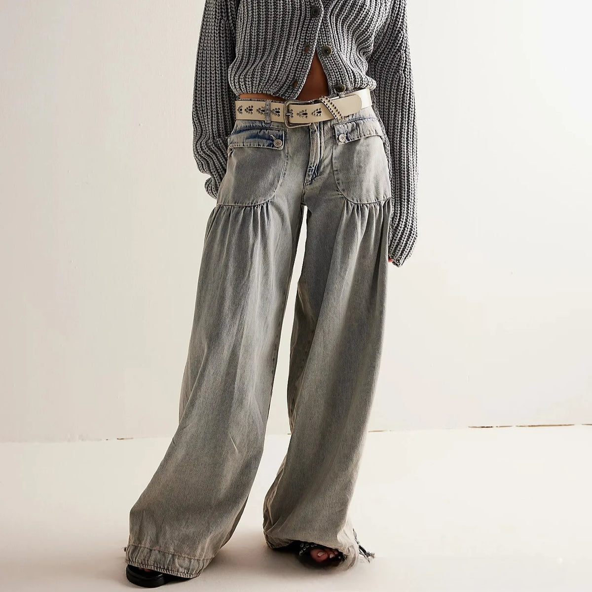 Front view of light grey washed denim wide-leg trousers with gathered pockets, styled with a chunky knit cardigan