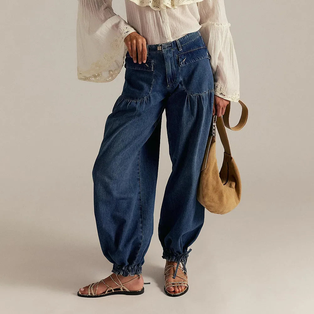 Close-up back view of grey denim trousers showing the drawstring hem and relaxed leg shape near ankle boots