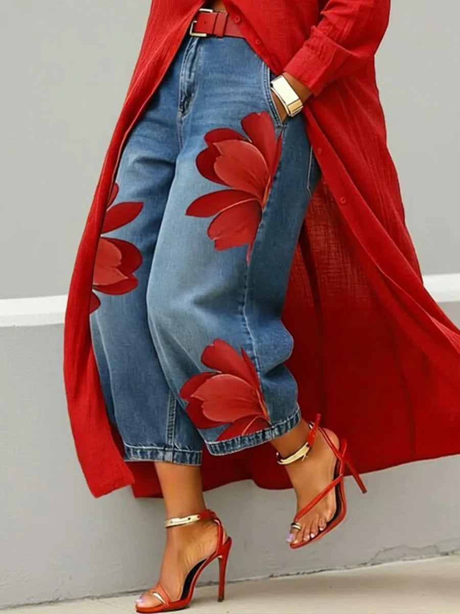 Woman in a red duster coat pairs it with high-waisted denim wide leg trousers featuring a large red floral print down one leg