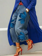 Blue duster coat styled with wide leg denim trousers showing a bold blue floral print running along the thigh and hem
