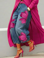 Close-up of wide leg denim trousers with a vivid rose red floral print along the leg, paired with a magenta coat and matching heels