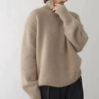 Side view of a beige polo neck jumper with ribbed high collar and oversized sleeves worn over black trousers