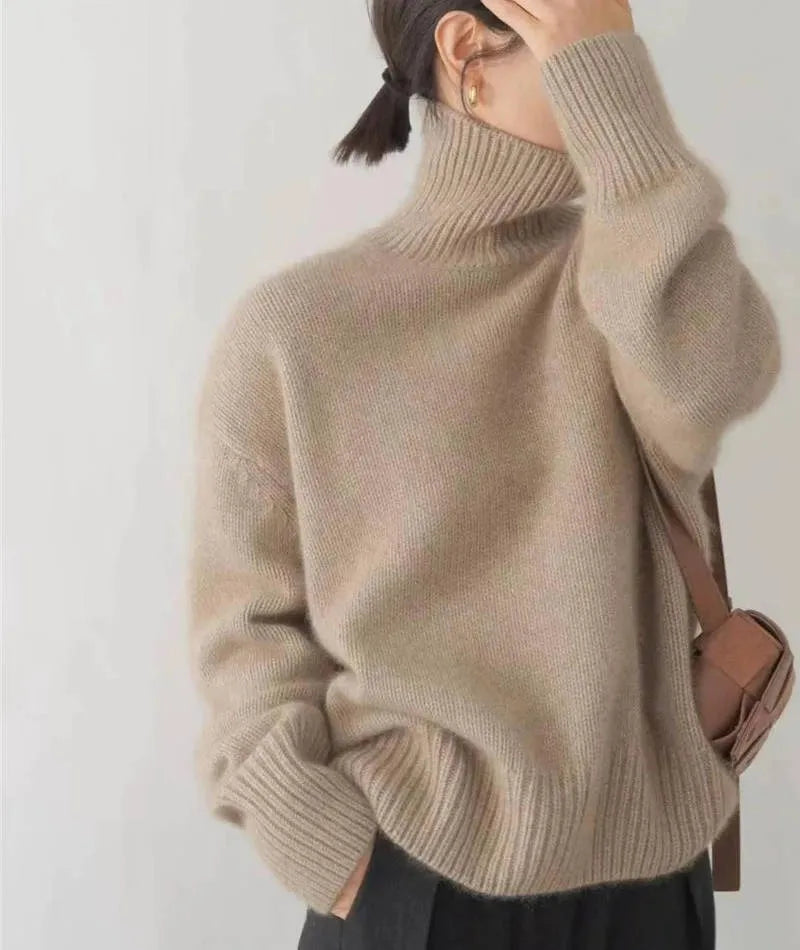 Front view of a beige cashmere-style jumper with model's hand resting on the ribbed polo neck collar