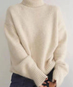 Cream jumper with rolled ribbed collar and dropped shoulder seams, paired with dark denim jeans