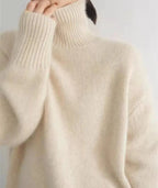 Close up of ribbed cuff and collar detail on a cream polo neck jumper against a plain background