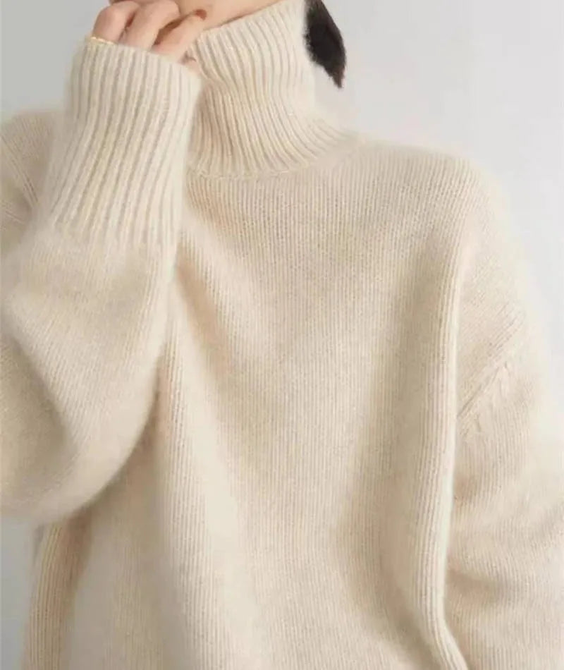 Close up of ribbed cuff and collar detail on a cream polo neck jumper against a plain background