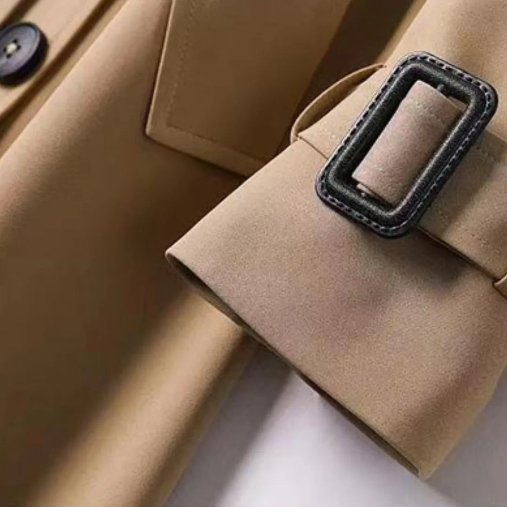 Camel trench coat detail showing the buckled cuff strap and dark button fastening