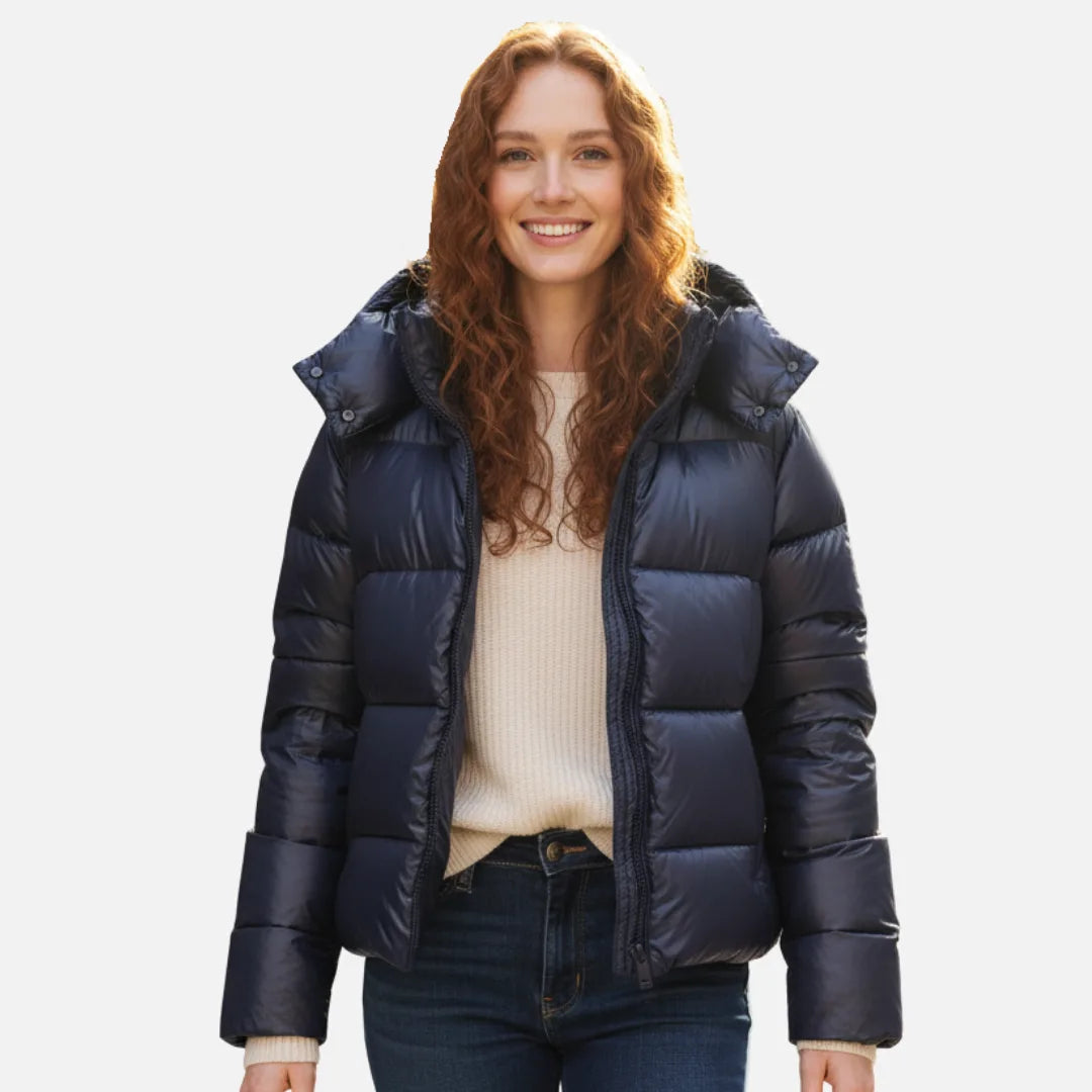 Woman wearing a glossy navy hooded puffer jacket, unzipped over a cream jumper and dark jeans, front view