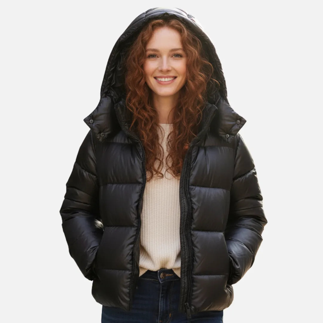 Woman wearing a glossy black hooded puffer jacket with the hood up, zipped over a cream jumper