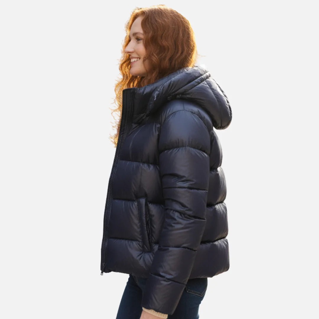 Side profile of a woman in a navy quilted puffer jacket showing the hood and slip pocket detail
