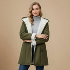 Front view of the olive green duffle coat with arms crossed, showing the cream fleece cuffs and hood