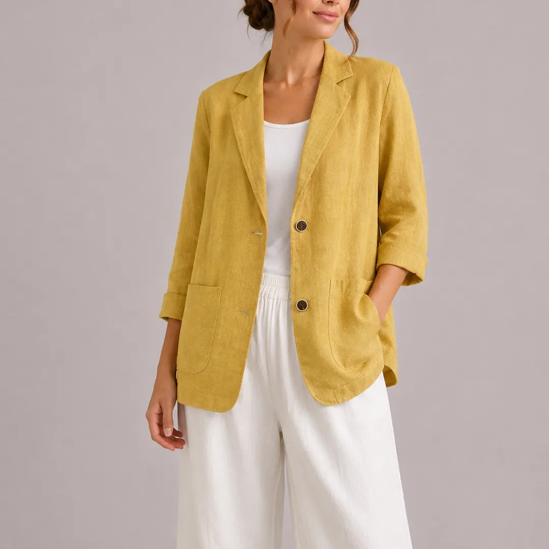 Model wearing a mustard yellow linen blazer with lapel collar and dark button fastening, paired with white trousers