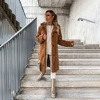 Close-up of a tan teddy coat with black button closure, styled with a cream jumper and white crossbody bag