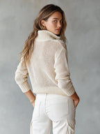 Back view of a beige open-knit jumper showing ribbed cuffs and the collar from behind