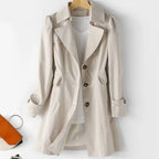 Beige single-breasted trench coat with front buttons and side pockets, styled over a white top and shorts